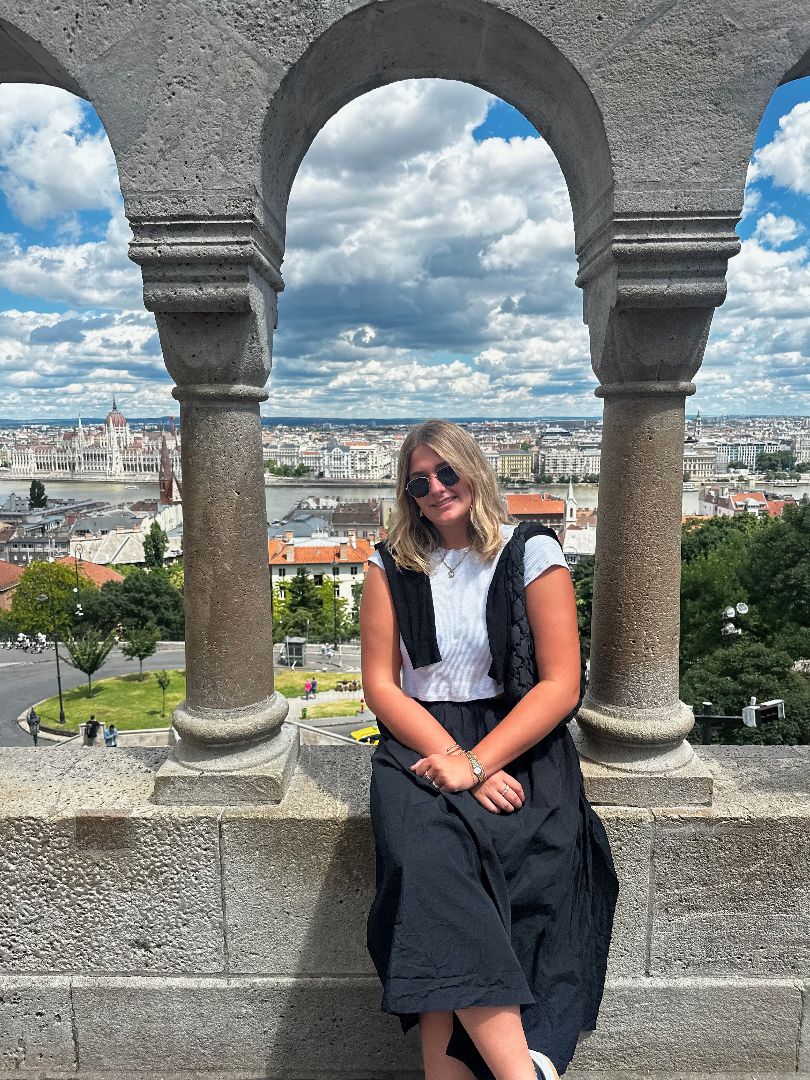 Zoe sitting on top of of a stone wall overlooking the city of Budapest