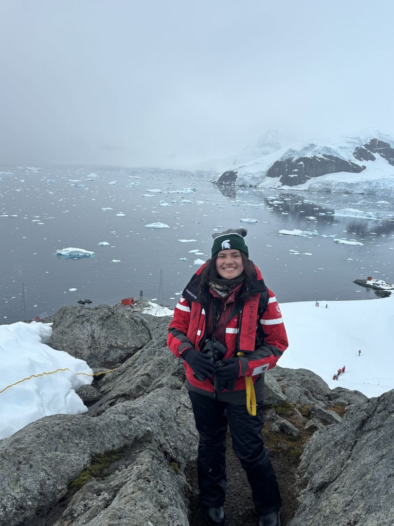 Paige wearing a Spartan winter hat and a red coat on the coast of Antarctica