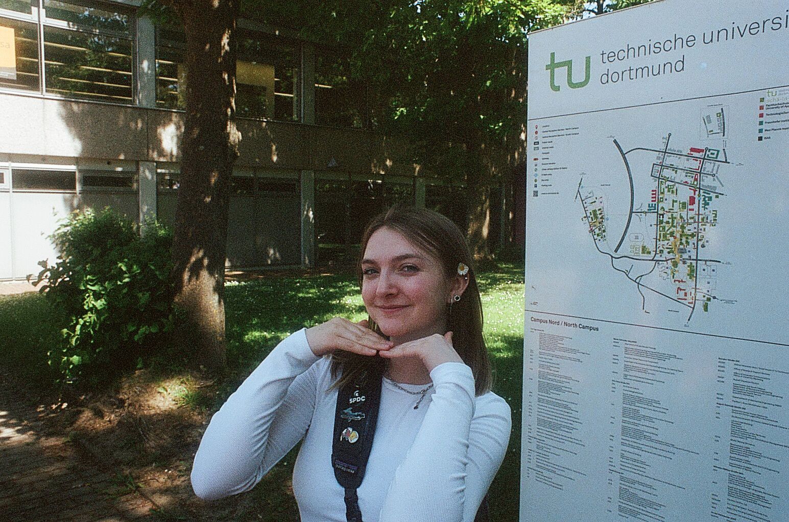 Tess holding her hands under her chin next to a TU Dortmund sign