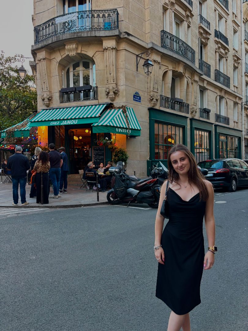 Jovana wearing a black dress standing in the street outside a Paris cafe