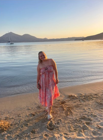 Emily in a pink dress standing on a beach in Greece