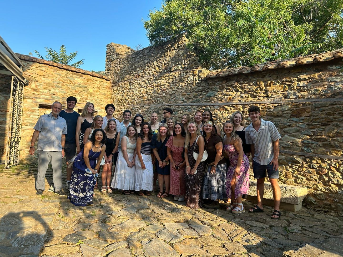 Group of students pose in front of a stone wall in Greece