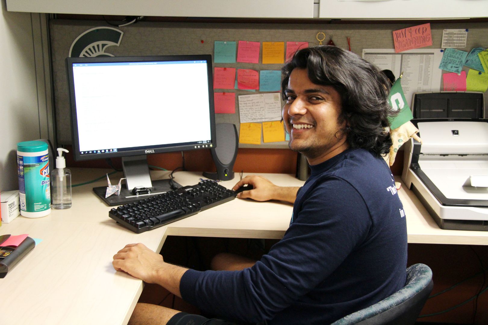 Abhimanyu Kinha sitting at desk in front of a computer. He is facing the camera and smiling. He works in the office of OISS in the MSU International Center.