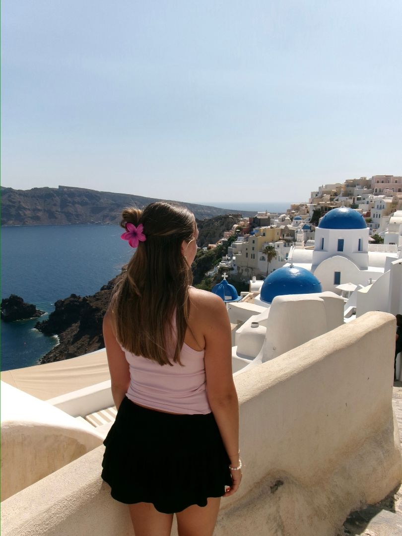 Capri on a stone balconly with a pink flower in her hair looking over the town of Santorini