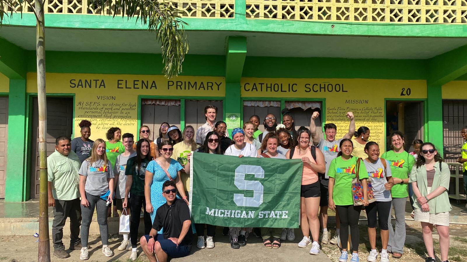 Group of MSU students holding Spartan flag in front of colorful building in Belize