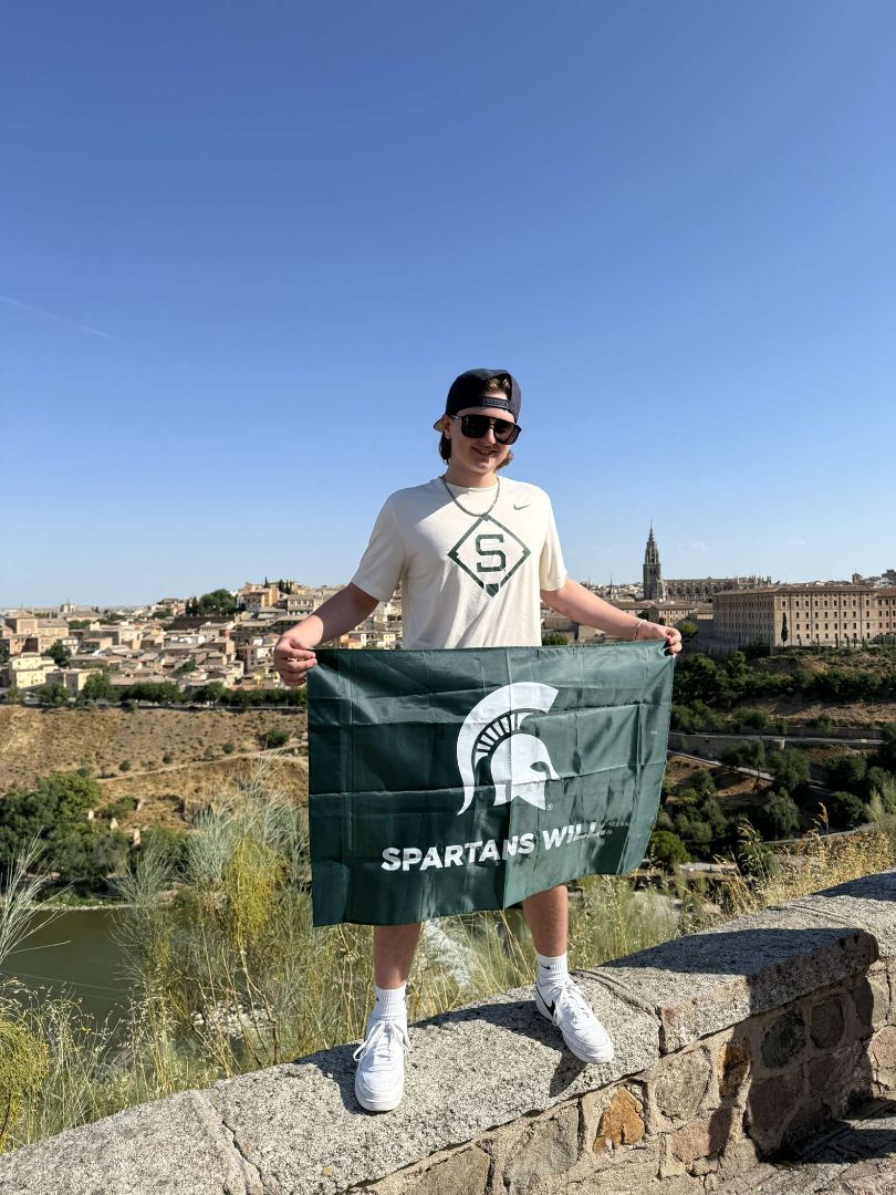 Adam standing on a stone wall holding a Spartan flag
