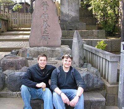 two men in front of monument with Japanese writing