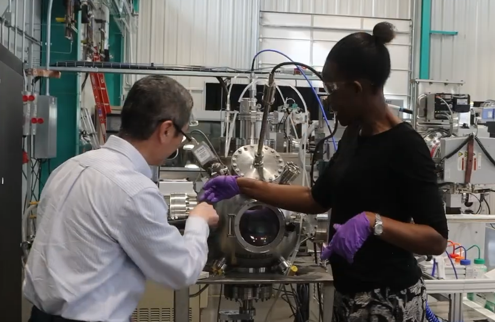 a man and woman in lab gear work on a machine