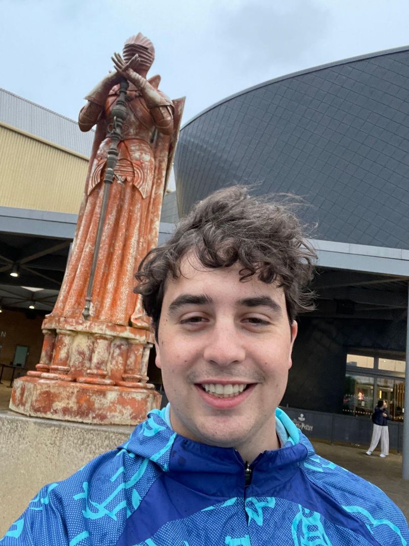 Cooper wearing a blue jacket standing in front of a statue in the UK