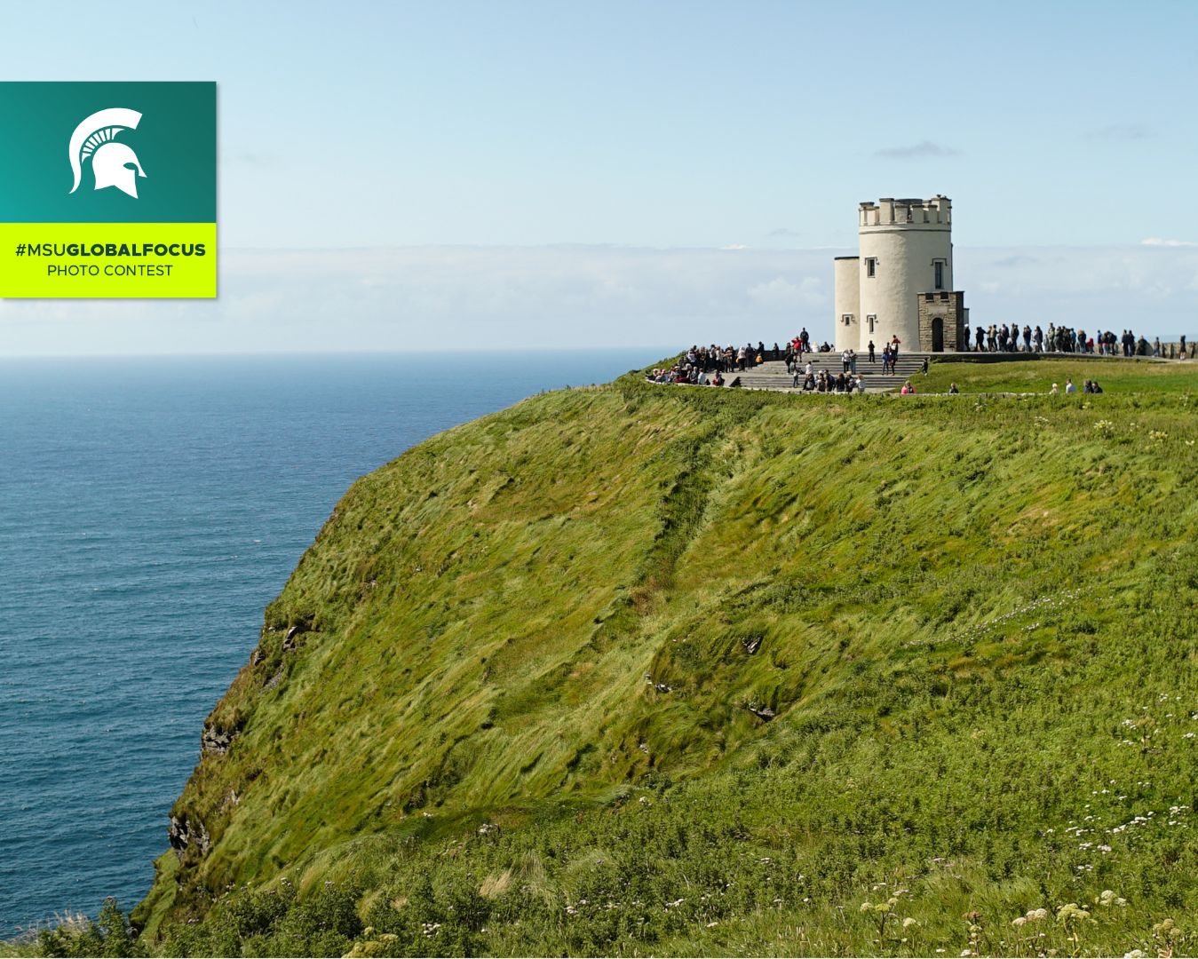 a castle on a cliff facing the ocean with many visitors looking out toward horizon