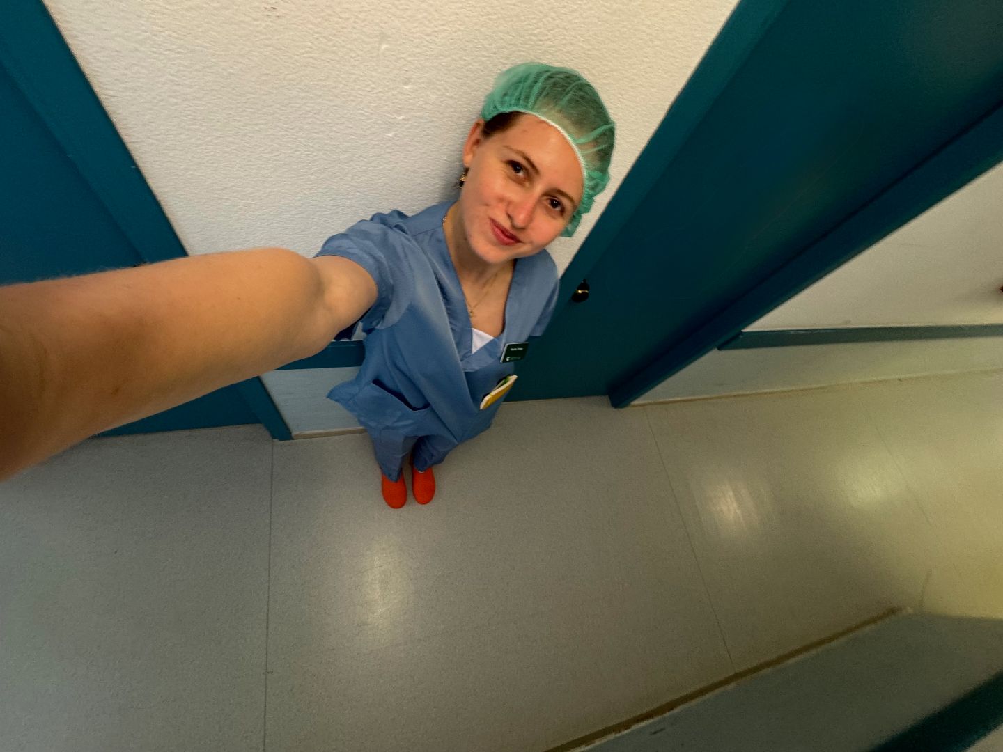 Monika wearing blue scrubs taking a selfie in a hospital hallway