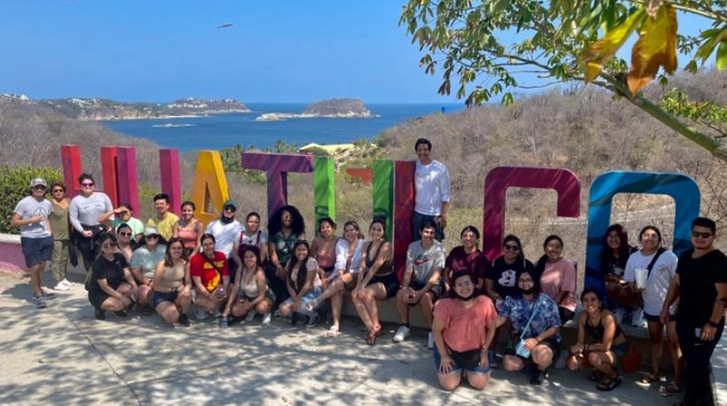 Group of MSU student sitting in front of colorful Huataluco sign in Mexico