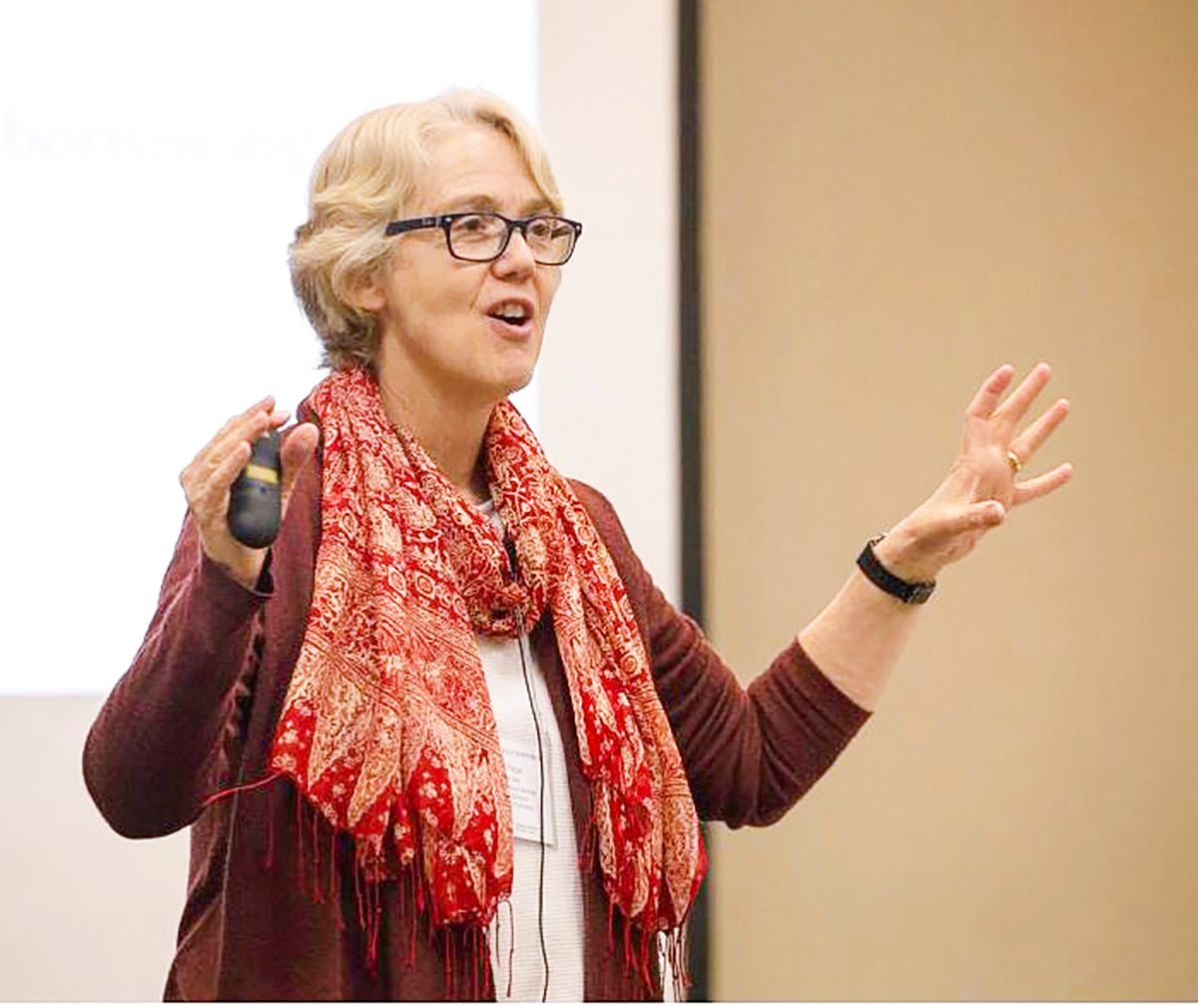 Lynne Paine in front of a projector screen, speaking and holding a PowerPoint clicker.