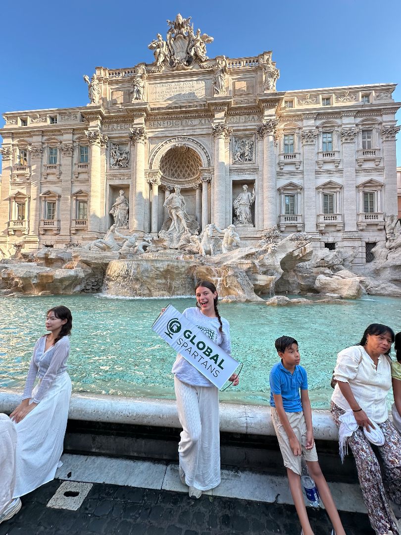 Flynn holding a Global Spartans banner in front of the Trevi Fountain in Rome