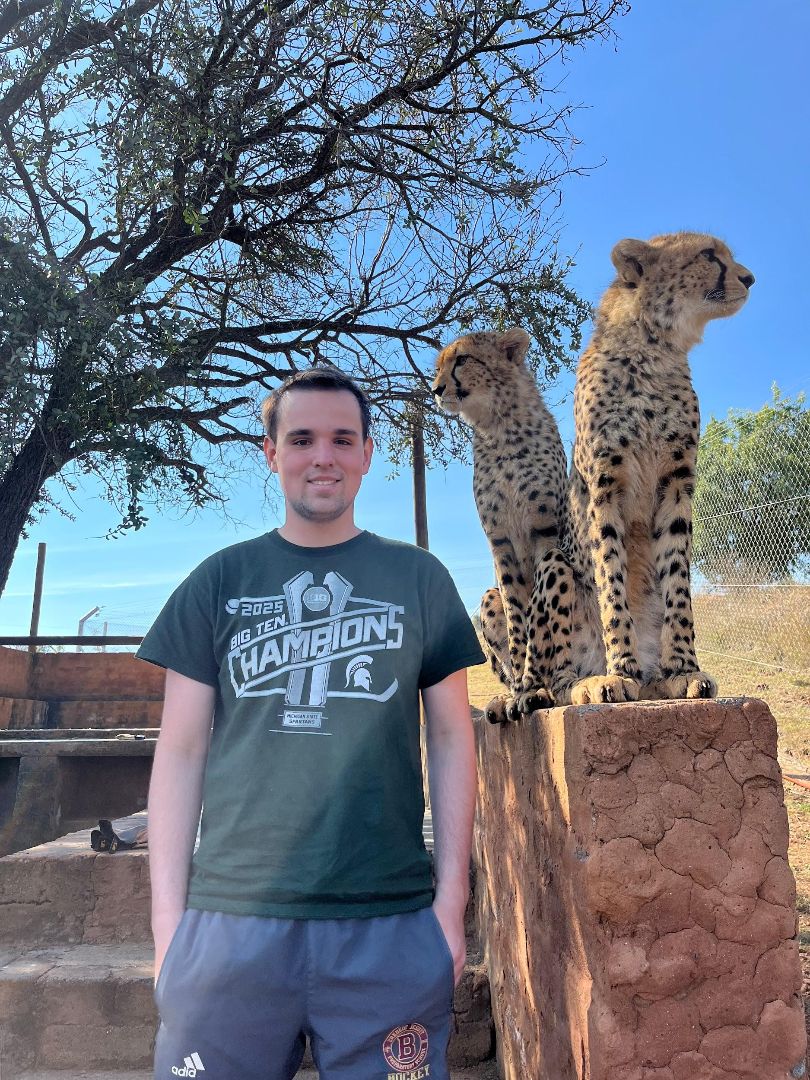 Kerem wearing an MSU tee shirt standing next to two cheetahs