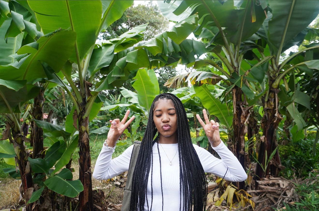 Brianna holding up peace signs with her eyes closed among large tropical plants