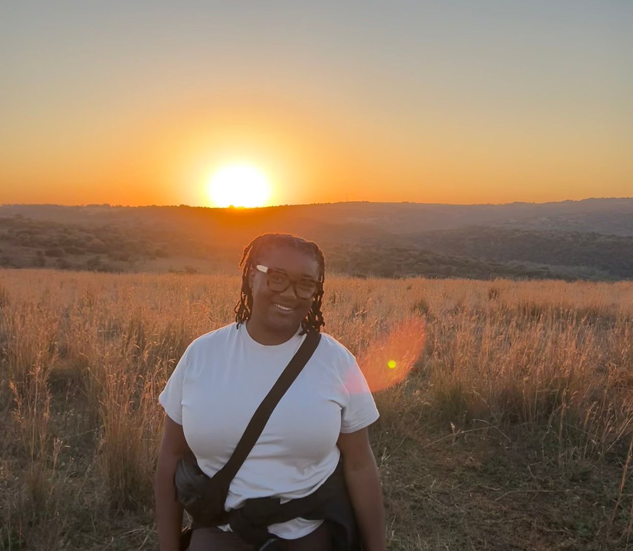 Joi wearing a white tee shirt standing in a field at sunset