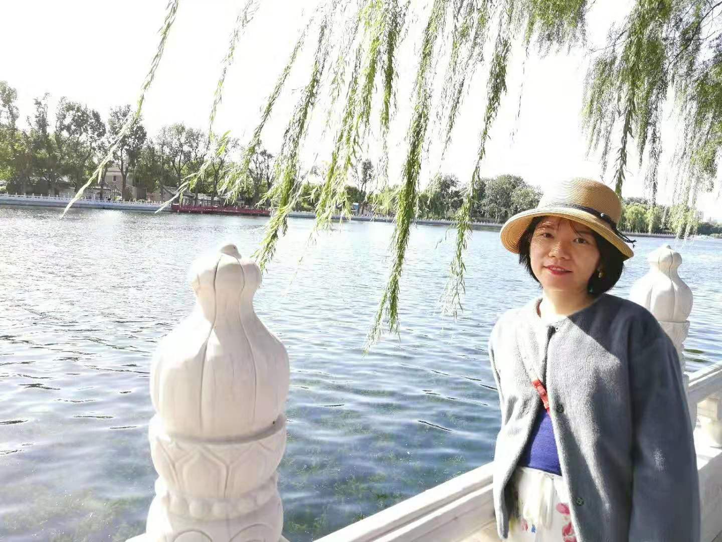On a sunny day, Jing poses, wearing a white hat, in front of Shicha lake in Beijing.
