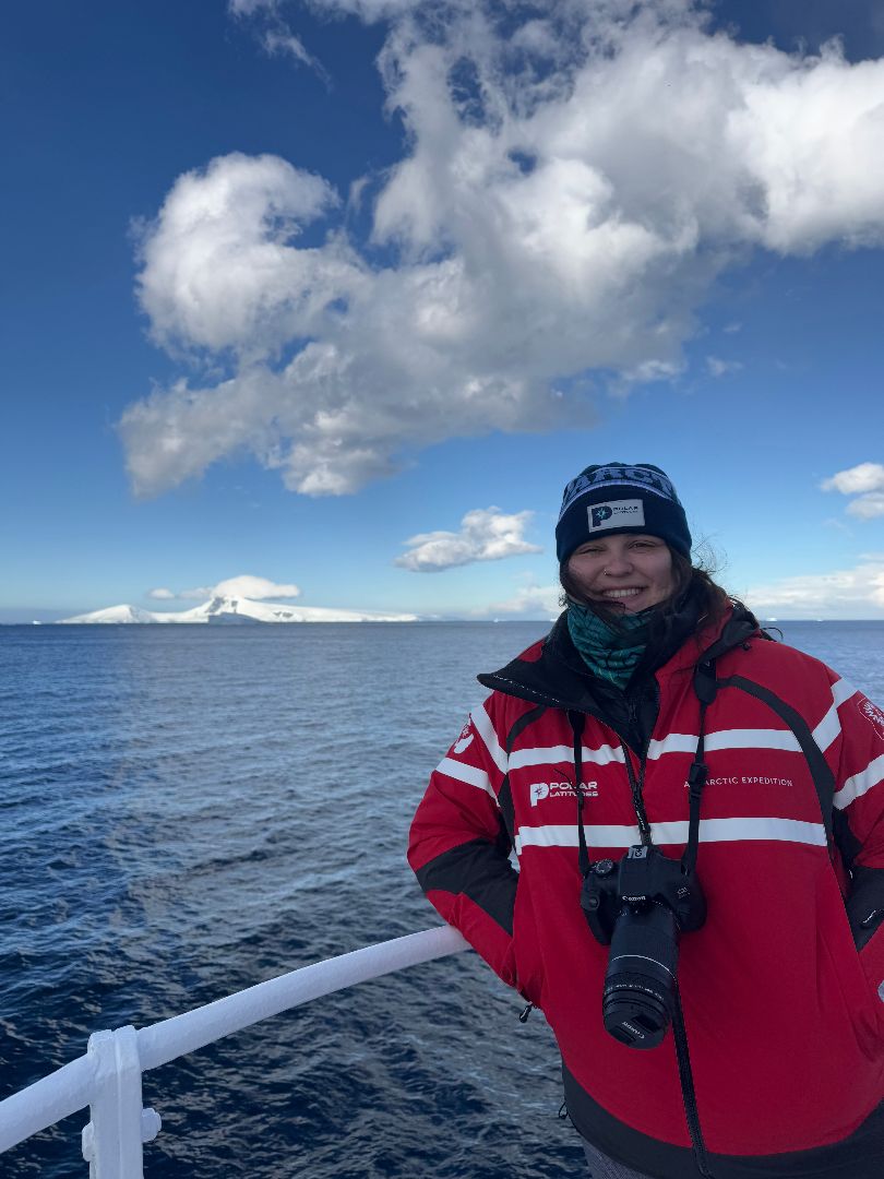 Kenna wearing a red coat with a camera around her neck ona ship in Antarctica