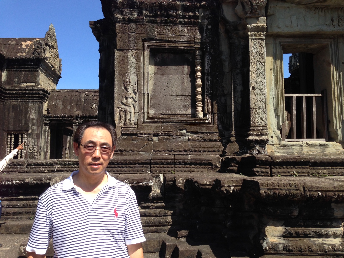 Dr. QI poses in front of an ancient stone building with blue sky in the background