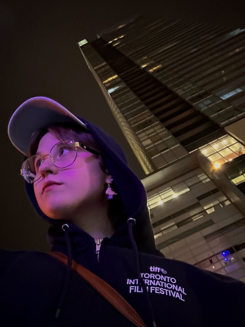 Madison wearing a black TIFF jacket and baseball hat at night in Toronto