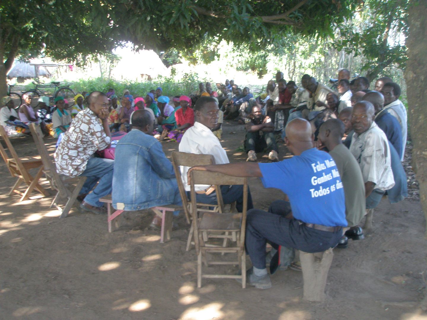 A group of Mozambique residents sit in chairs outside in a circle engaged in discussion.