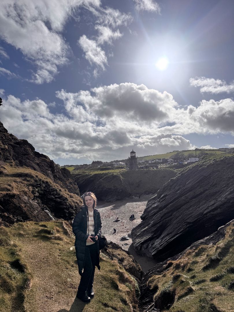 Lily standing on the rocky coast of Ireland with a light house in the background