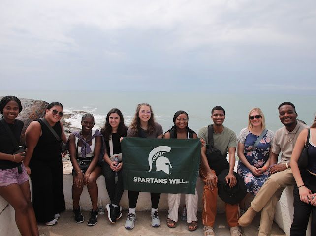 Group of students holding the Spartan flag on a balcony overlooking the ocean