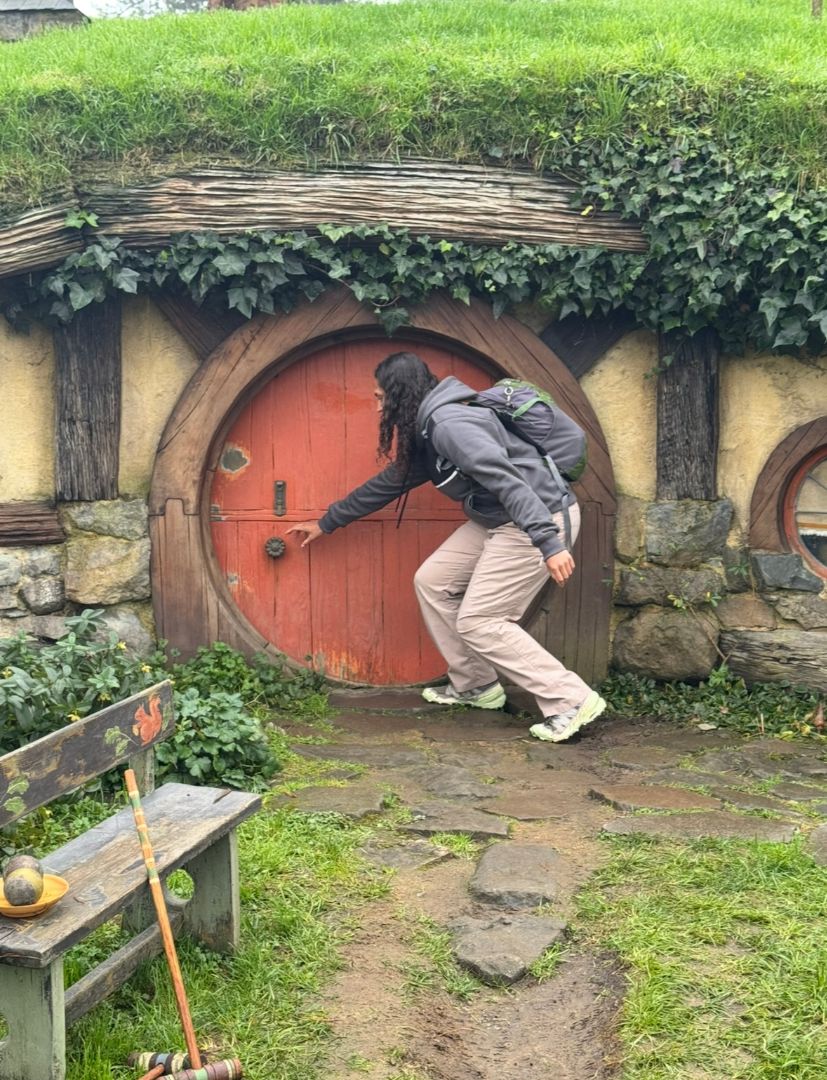 Madison reaching down to open a round hobbit door in New Zealand