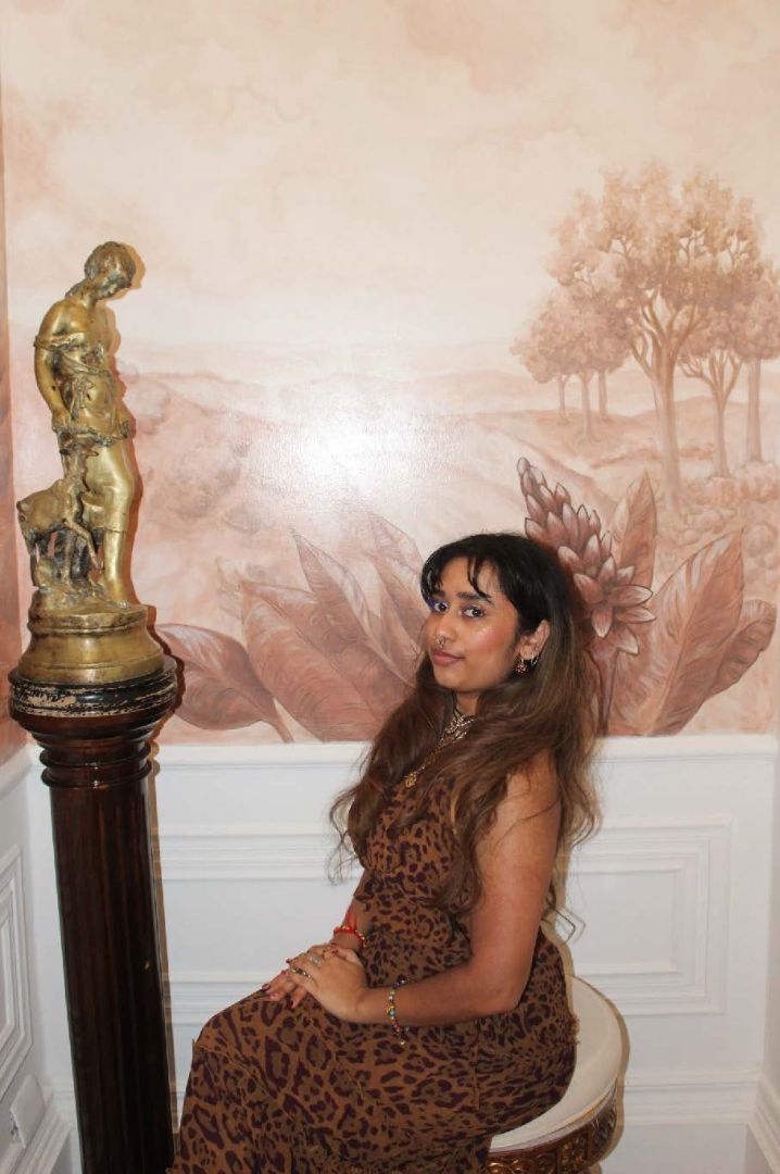 Niranjana sitting on a stool in front of a bronze sculpture