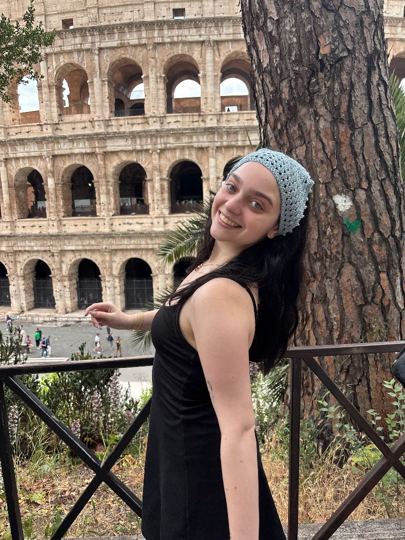 Maya posing in a black dress and light blue headband in front of the colesium in Rome