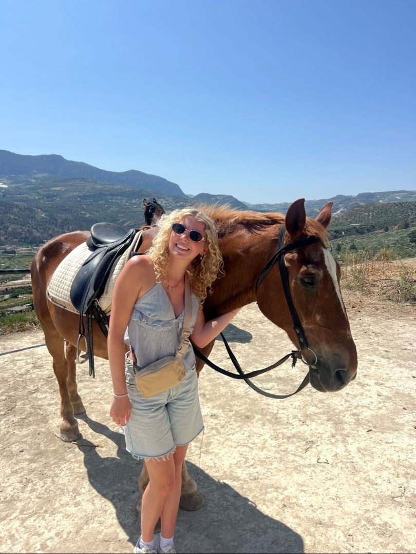 Natalie standing next to a brown horse on a mountain in Greece