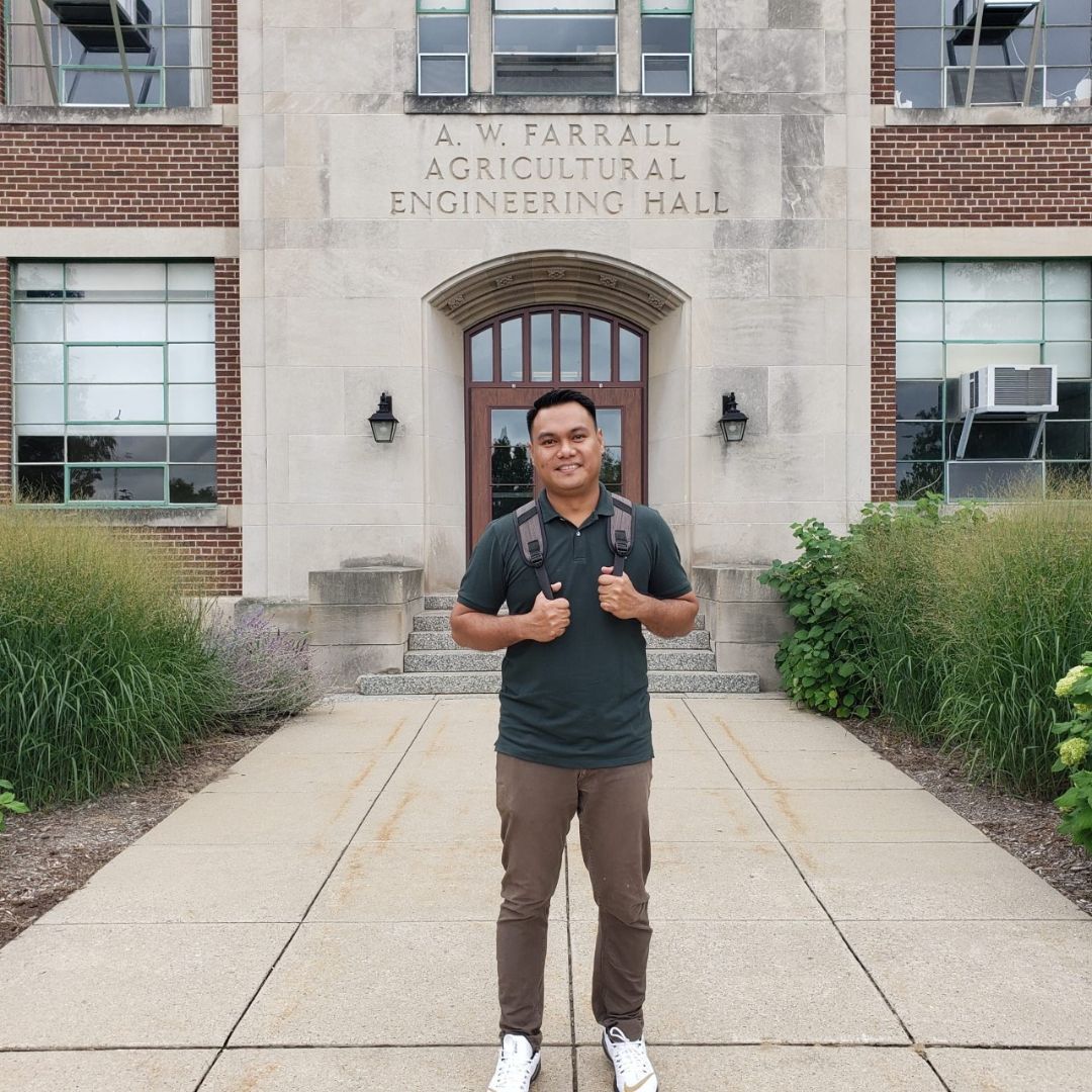 Image of a man wearing a green shirt and backpack in front of a brick building.