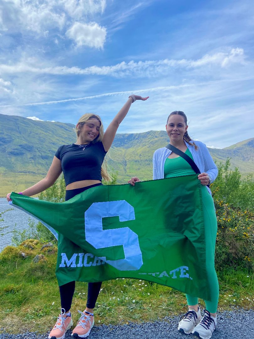 Cora and friend holding a Spartan flag with mountains in the background in Ireland