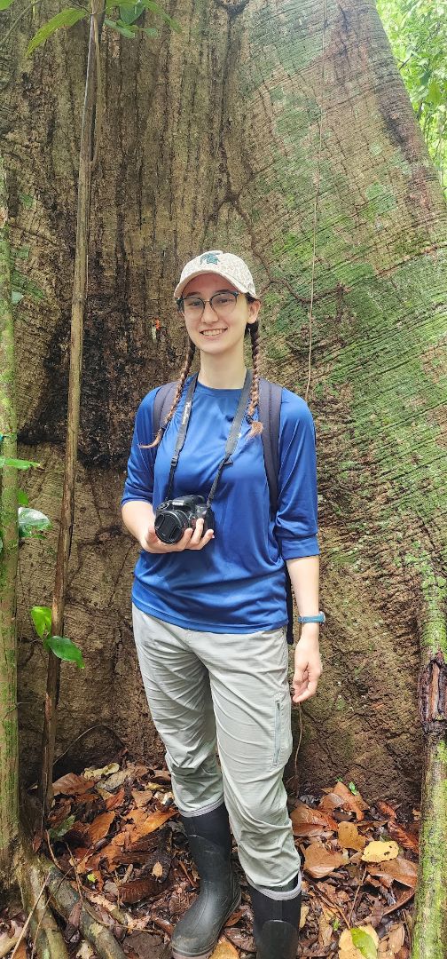 Marieke posing in front of a large tree trunk holding a camera around her neck in Panama