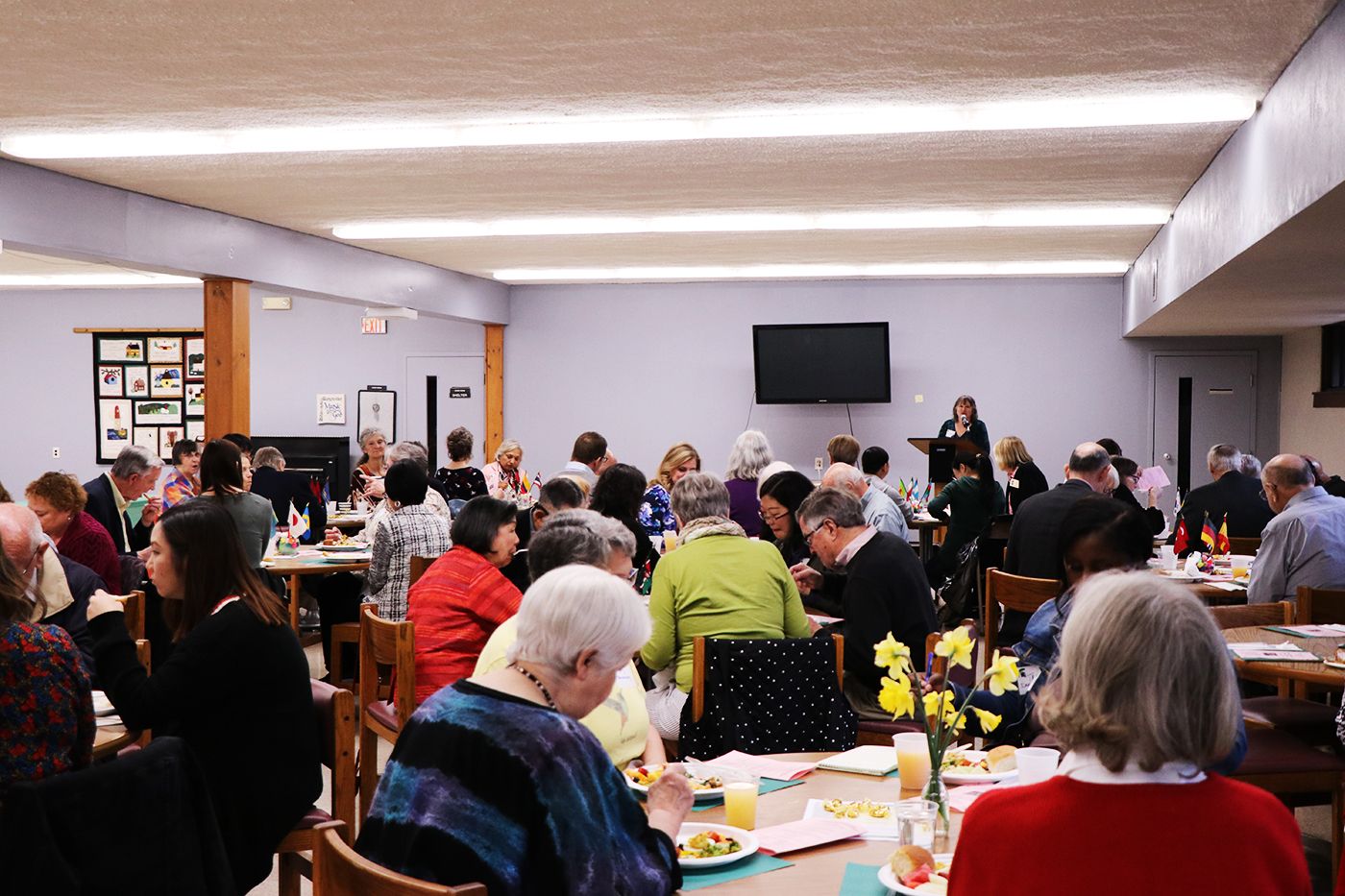 Tables filled with people sitting for luncheon. Woman at the podium is speaking to crowd.