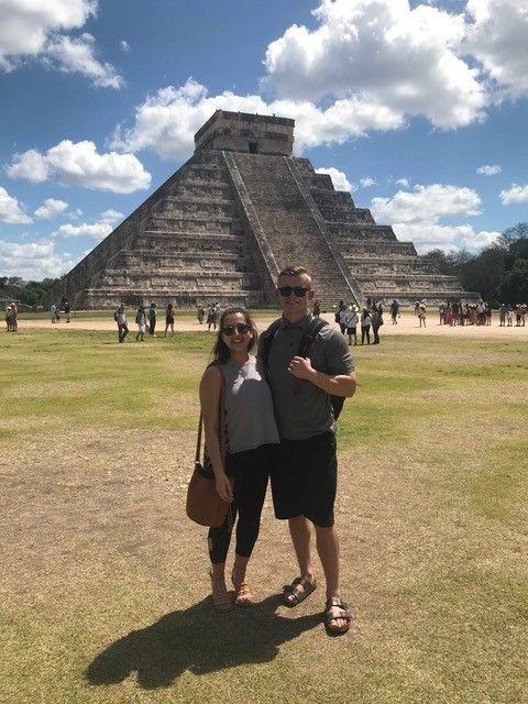 Holmes stands in front of a Mexican pyramid with a young woman.
