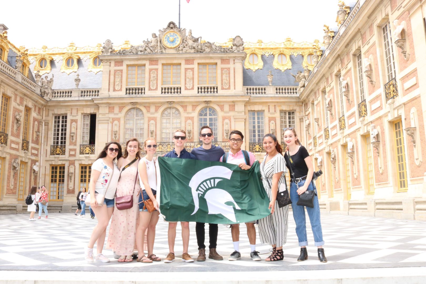 A group of students holding an MSU spartan flag outside in front of an ornate building