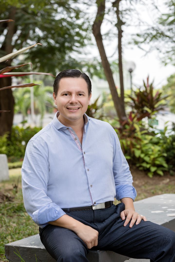 Headshot of Daniel Ortega Pacheco, sitting on a cement step, smiling at the camera