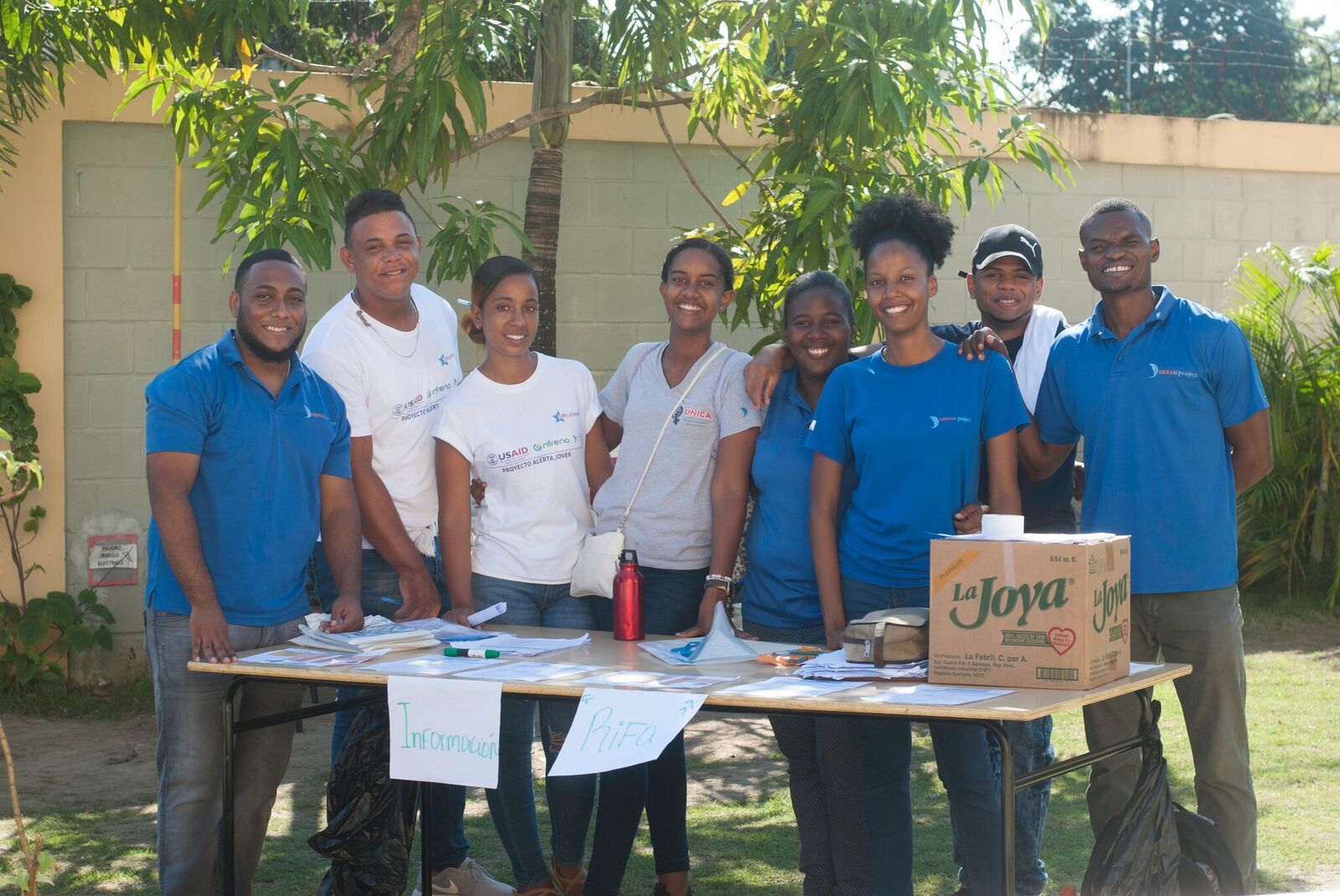 Eight young leaders stand behind a table, posing, at a community health fair