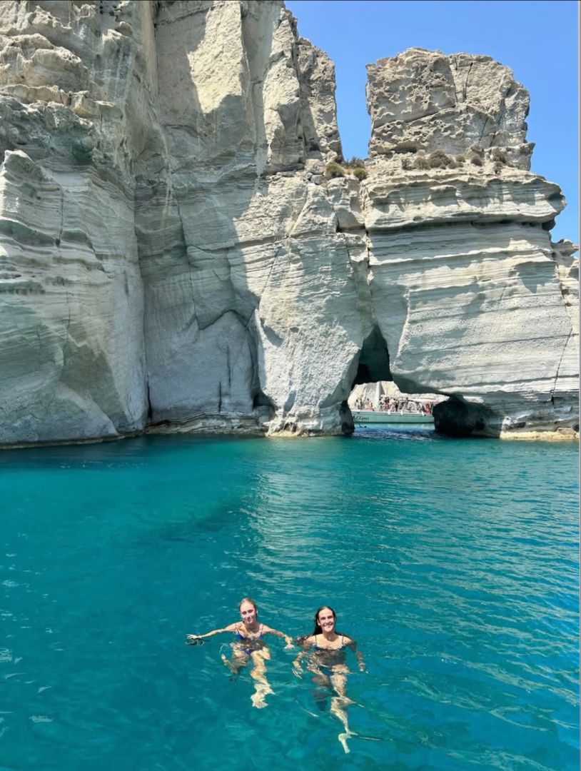 Mya and friend swimming in the sea with large rocks behind them