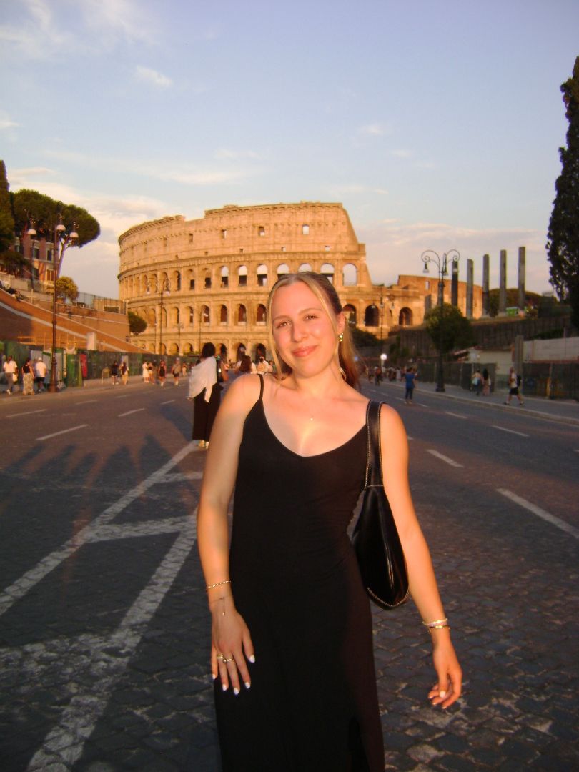 Corinne wearing a black dress posing on a street with the Roman colesium in the background