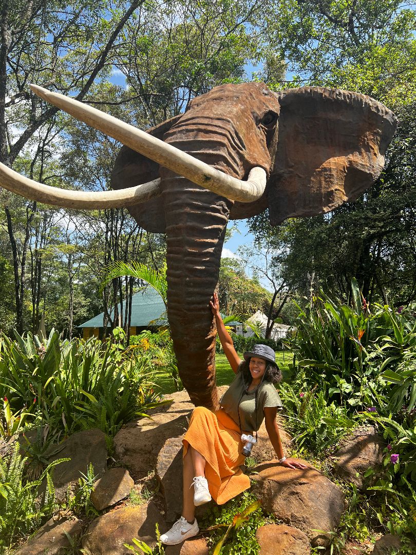 Lily sitting beneath a large elephant head statue in Kenya