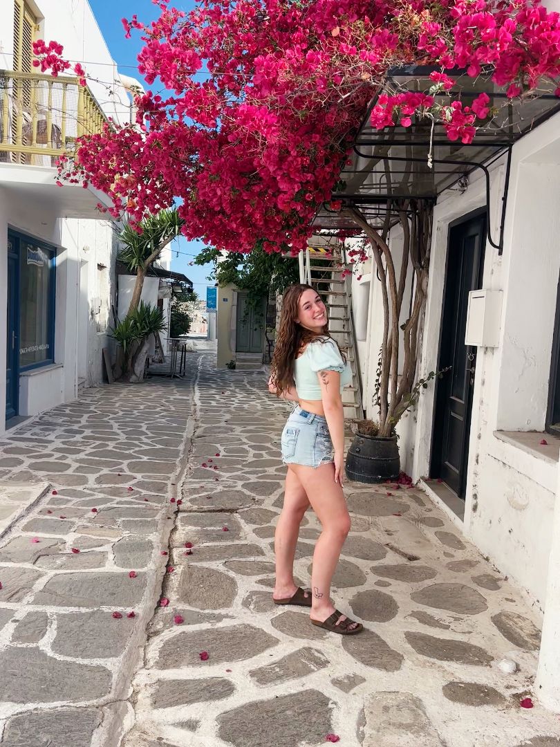 Faith standing on a narrow cobblestone street standing beneath bright pink flowers in Greece