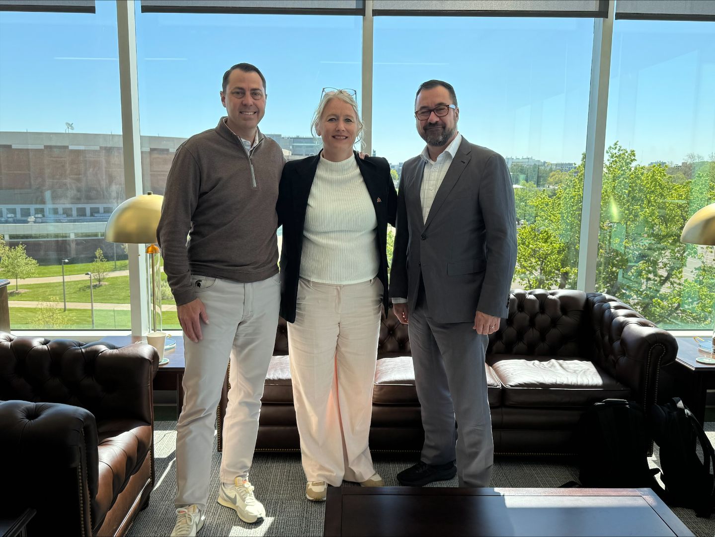 Vice Rector Gelineau and Julie Dionne posing for a photo with J Batt in his office. The Breslin Center is visible in the background.