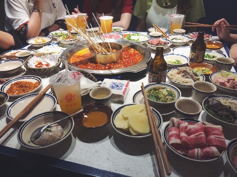 Table of boiling hotpot broth with many raw dishes.