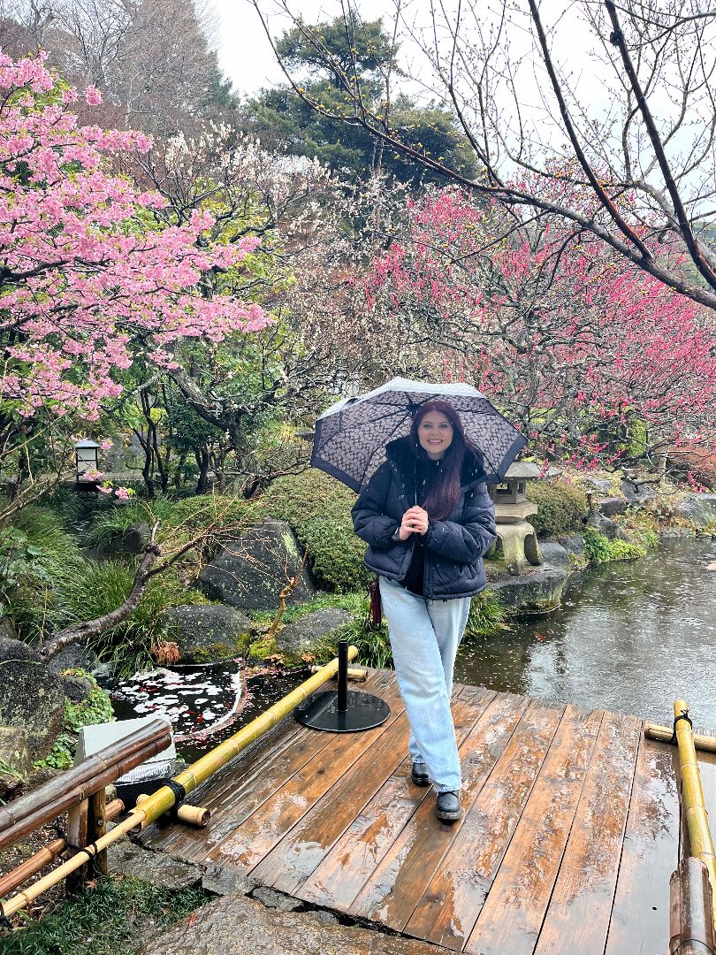 Kylie standing in a Japanese garden in the rain holding an umbrella