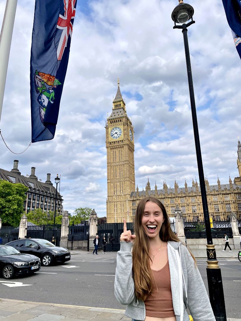 Joanna posing in front of Parliament pointing to Big Ben in London