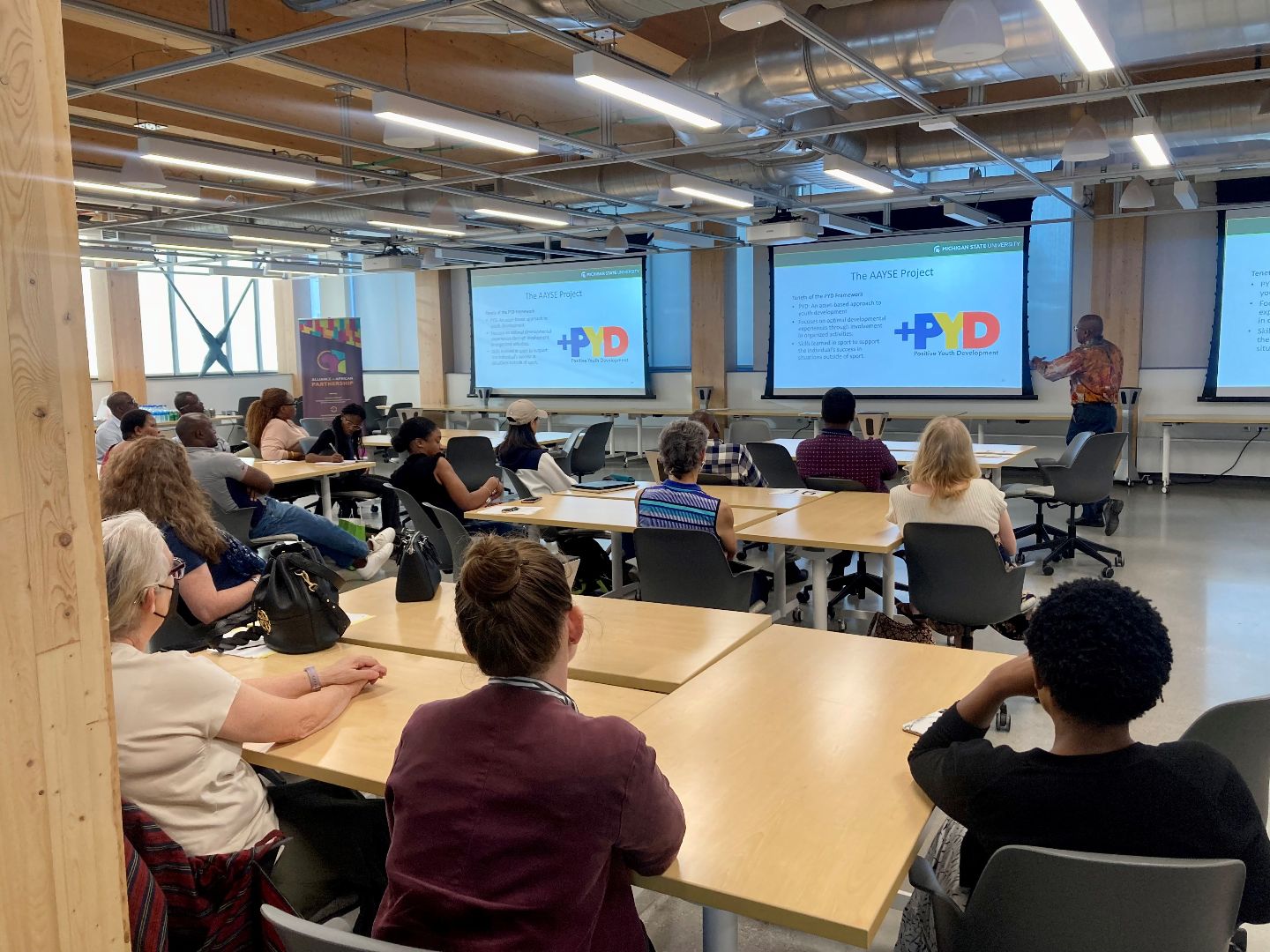 A classroom full of people look ahead at Dr. Leps Malete presenting findings from the group's research project. 