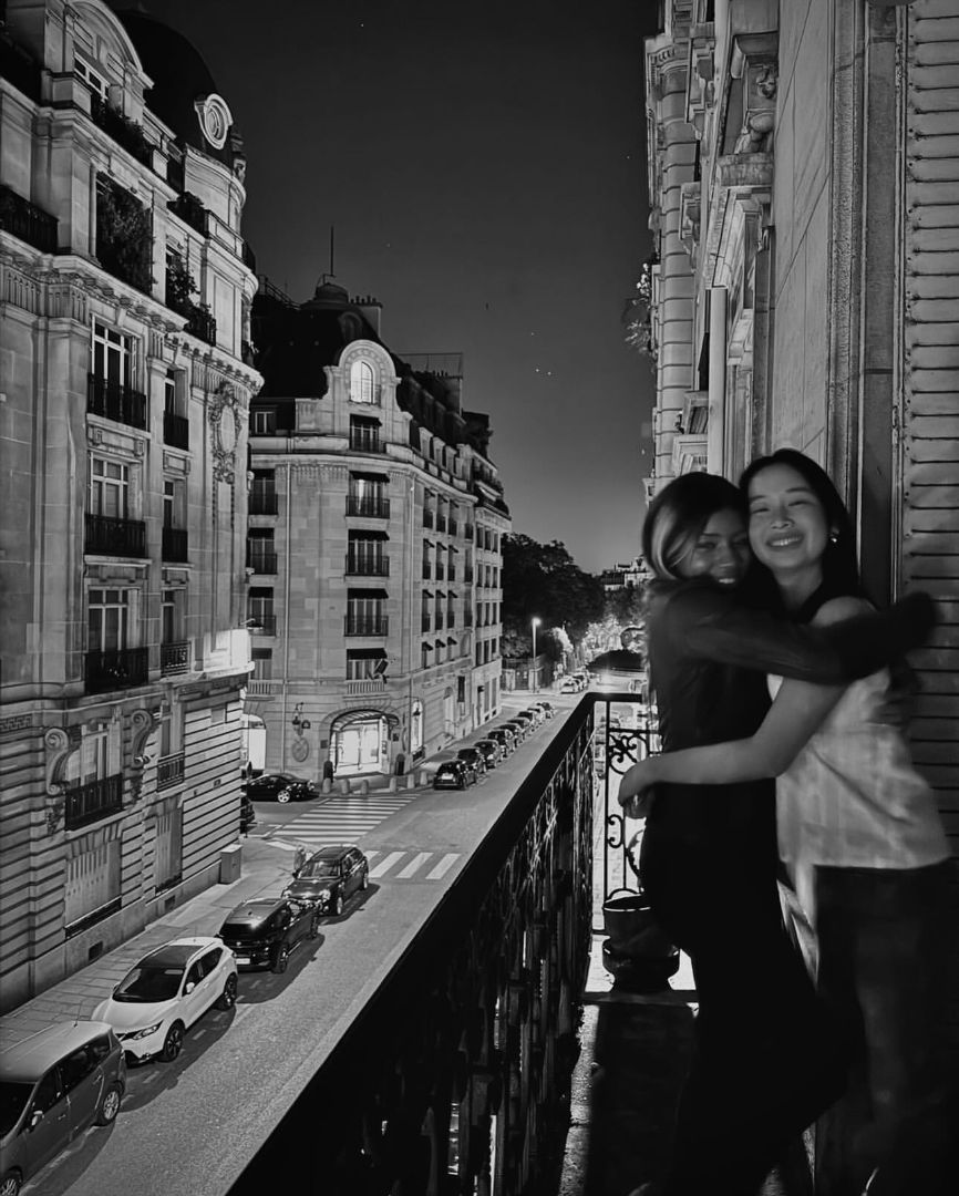 Black and white photo fo Mina and friend hug on a balcony at night in Paris 